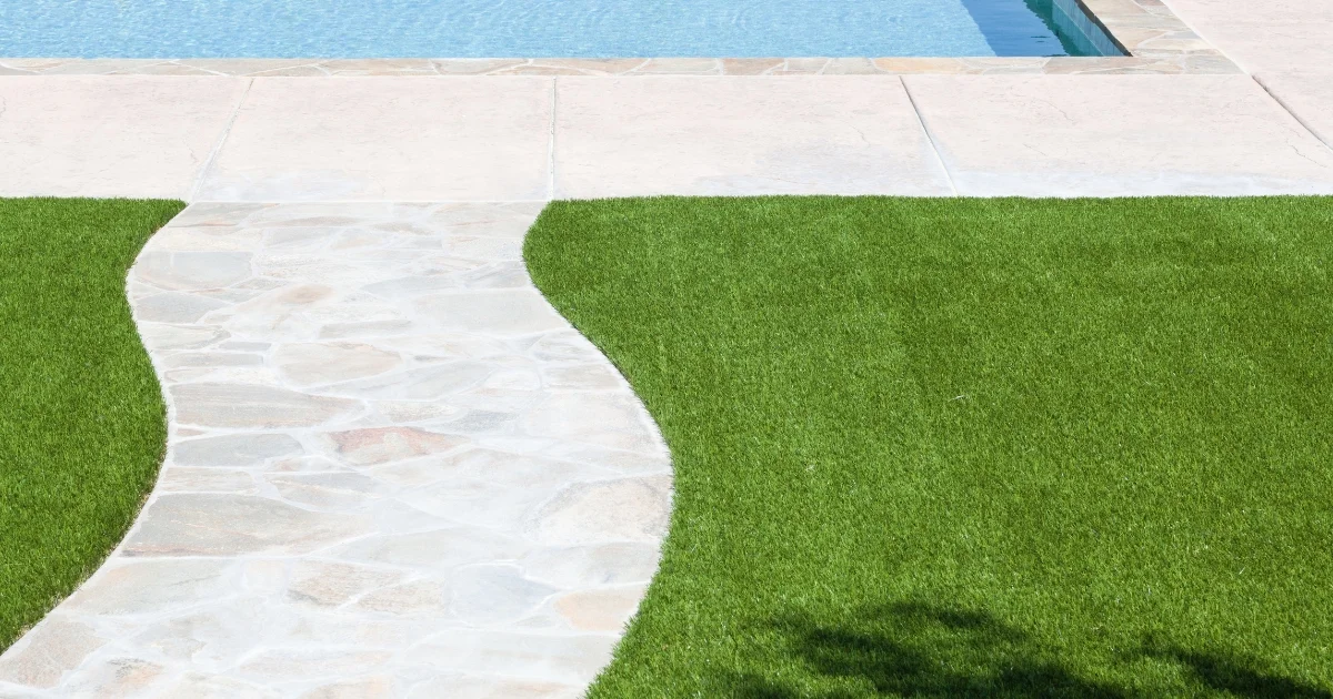 Curved stone walkway leading to a pool surrounded by artificial grass.